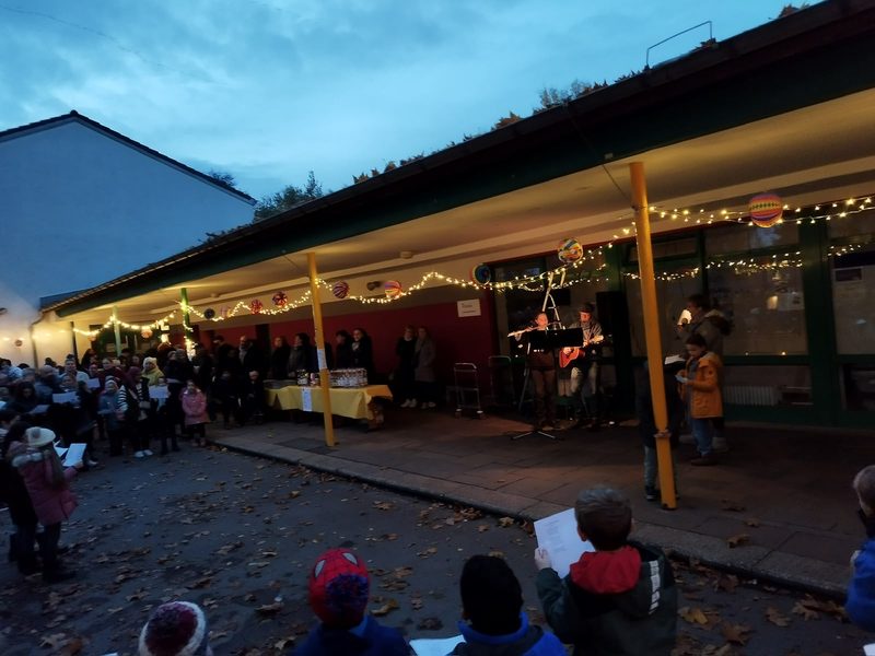 Abendliche Versammlung vor der Schule unter Lichterketten und Lampions