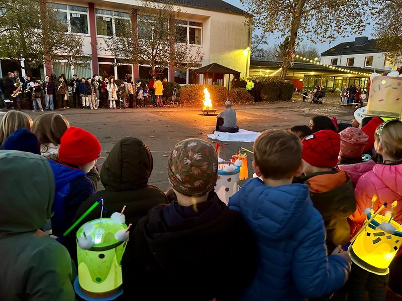 Kinder mit leuchtenden Laternen rund um das Martinsfeuer auf dem Schulhof