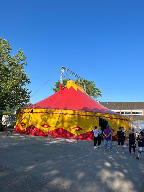 Kinder stehen vor dem rot-gelben Zirkuszelt auf dem Schulhof